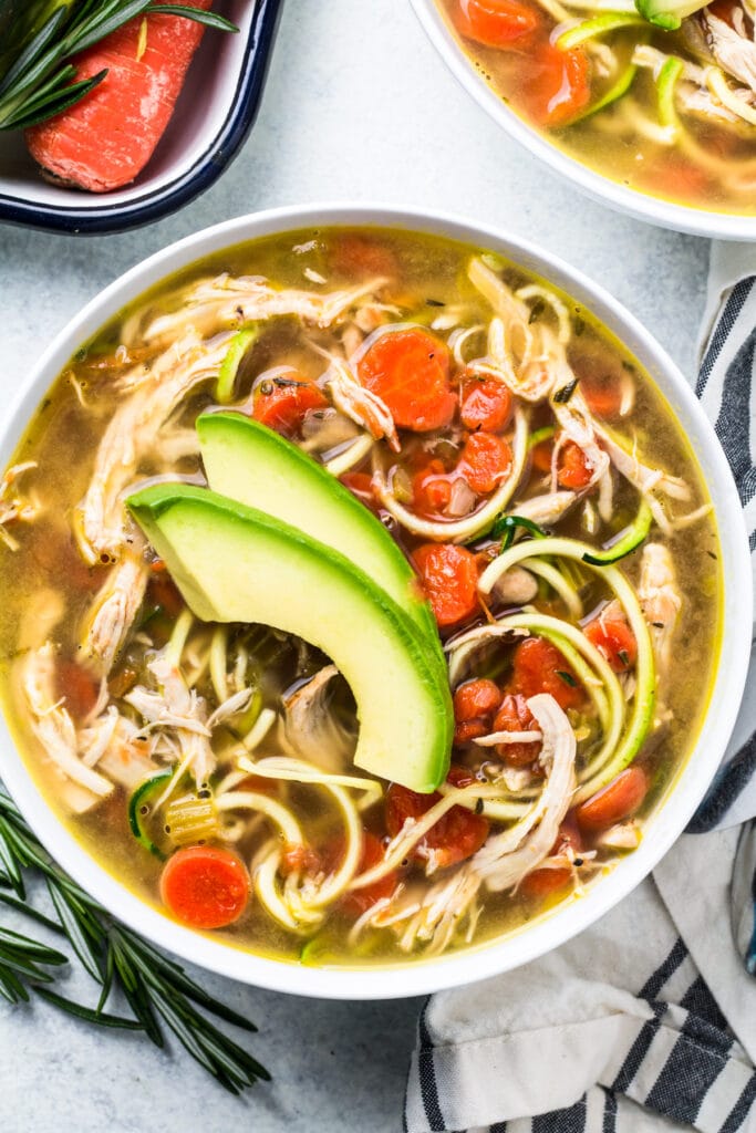 A close up overhead shot of paleo chicken soup in a white bowl on grey background
