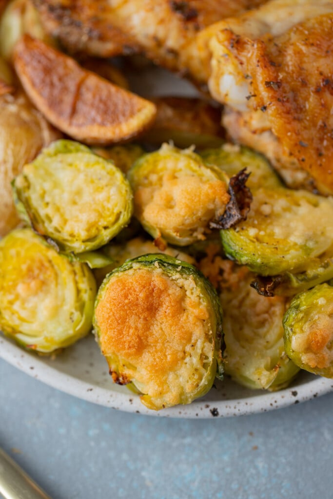 A close up of parmesan brussel sprouts on a plate with potatoes and chicken on the plate too