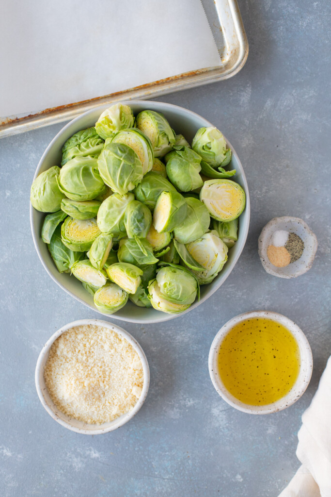 Ingredients for parmesan brussels sprouts in white bowls: brussels sprouts, olive oil, salt, pepper, garlic powder, parmesan cheese