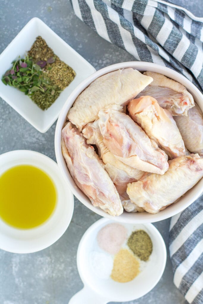 Ingredients for garlic parmesan chicken wings in small white bowls - wings, olive oil, spices and cheese