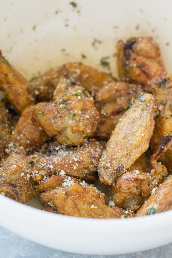 Parmesan Chicken Wings being tossed with parmesan cheese in a white bowl.