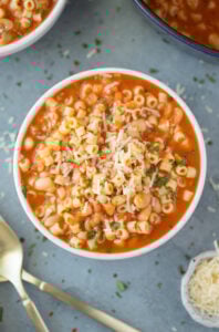 An overhead shot of a bowl of Pasta Fagioli with a bowl and pot to the side