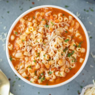 An overhead shot of a bowl of Pasta Fagioli with a bowl and pot to the side