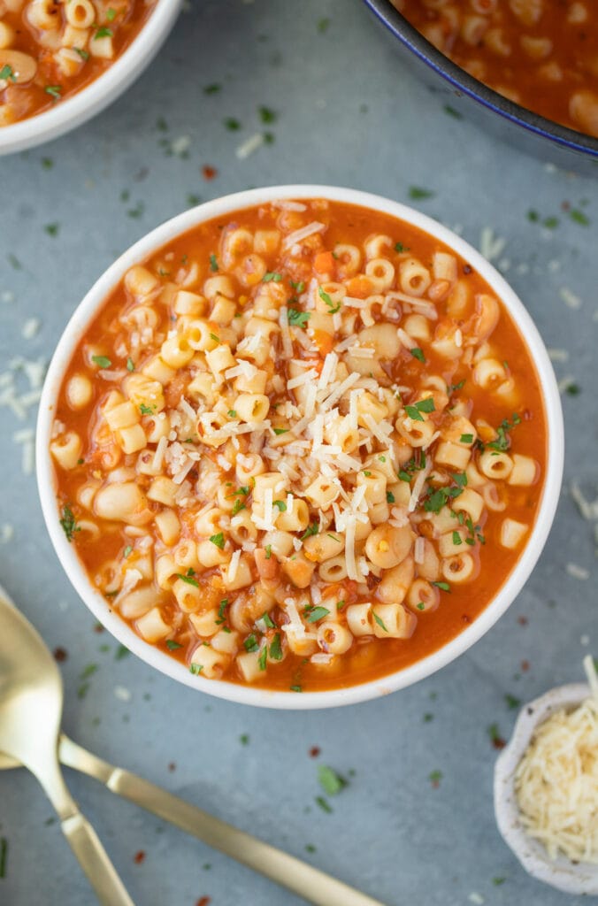 An overhead shot of a bowl of Pasta Fagioli with a bowl and pot to the side