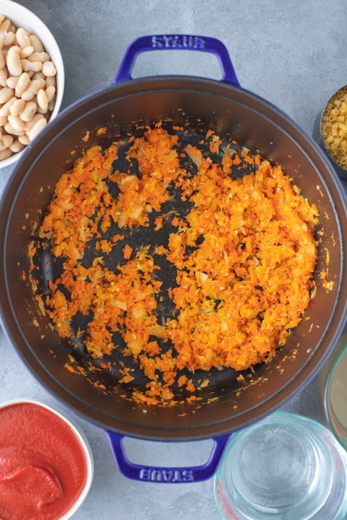 Veggies sauteing in a pot for easy pasta fagioli soup on a grey background