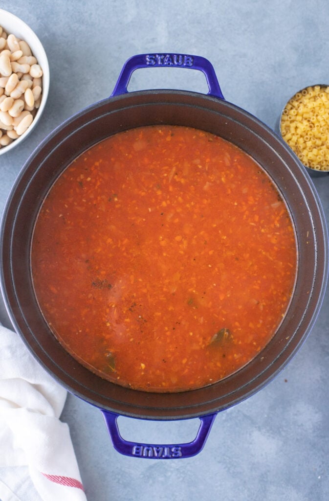 tomato sauce, spices, stock and water added to cooked veggies in a pot for pasta fagioli soup