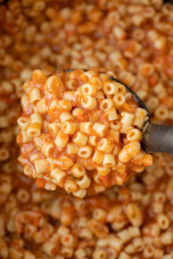 Cooked pasta fagioli in a pot with a ladle taking a large scoop out