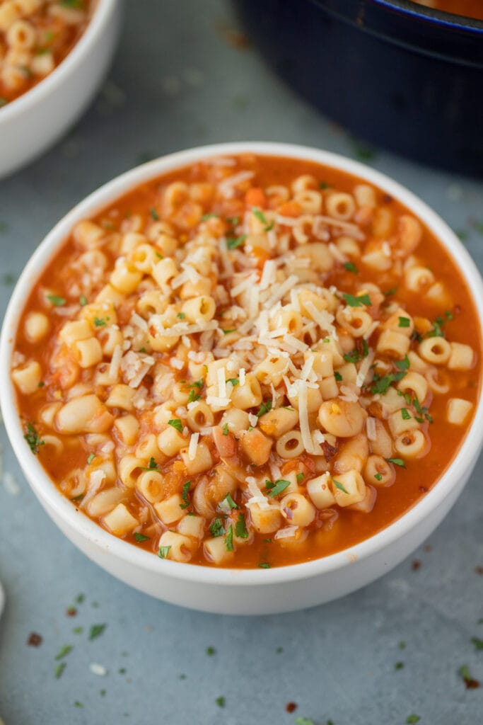 A white bowl of pasta fagioli with parmesan cheese on top