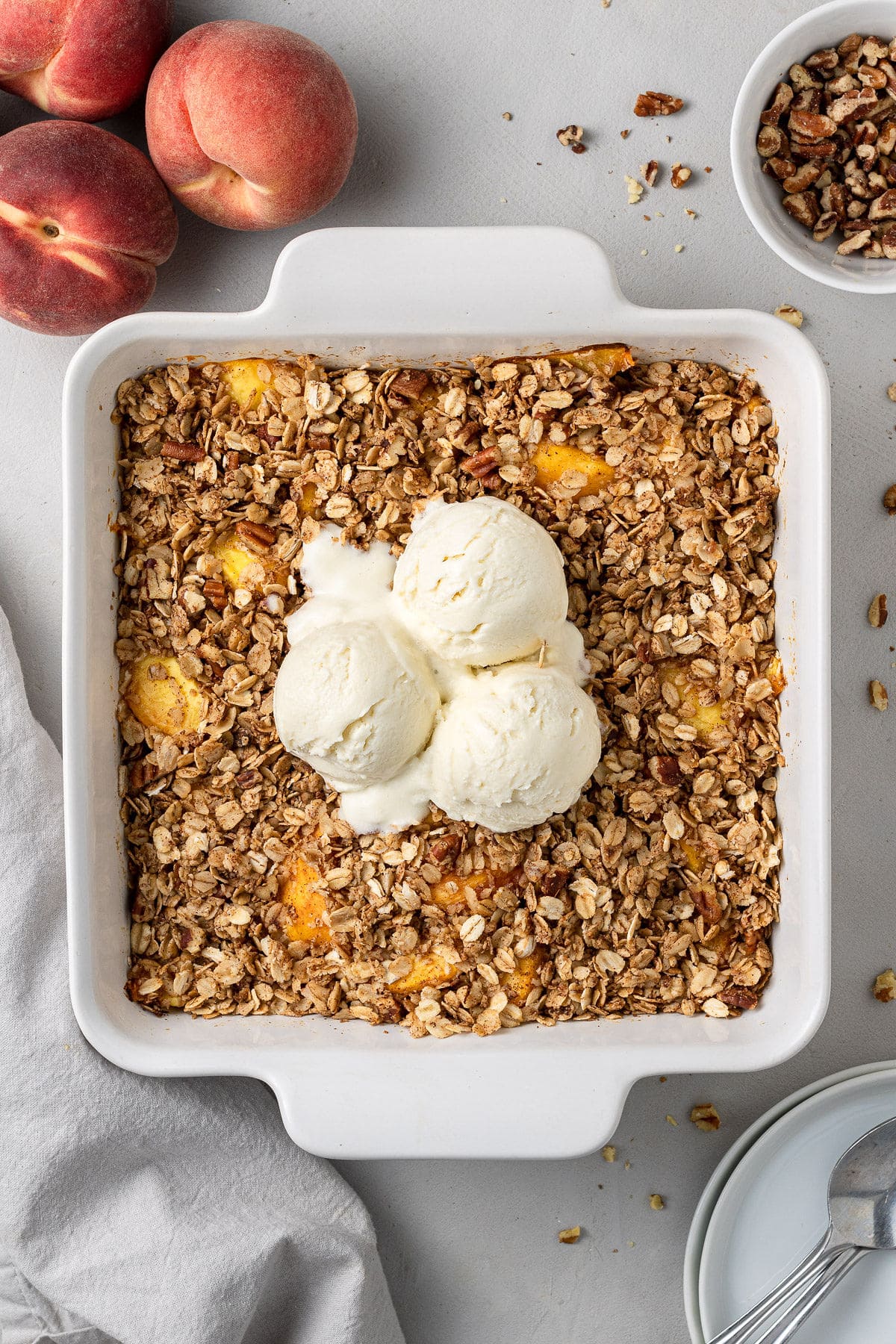 an overhead shot of healthy peach crisp in a white baking dish on a grey background