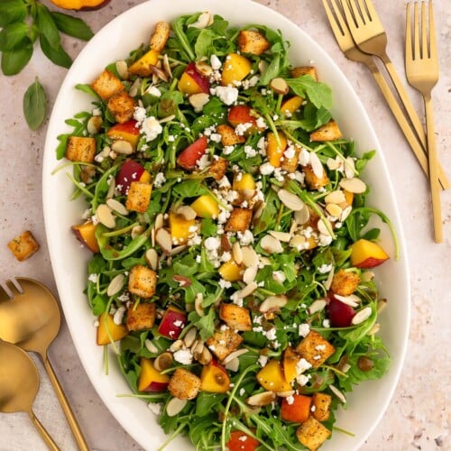 Peach Salad with goat cheese on a large white platter with more fresh peaches on the side.