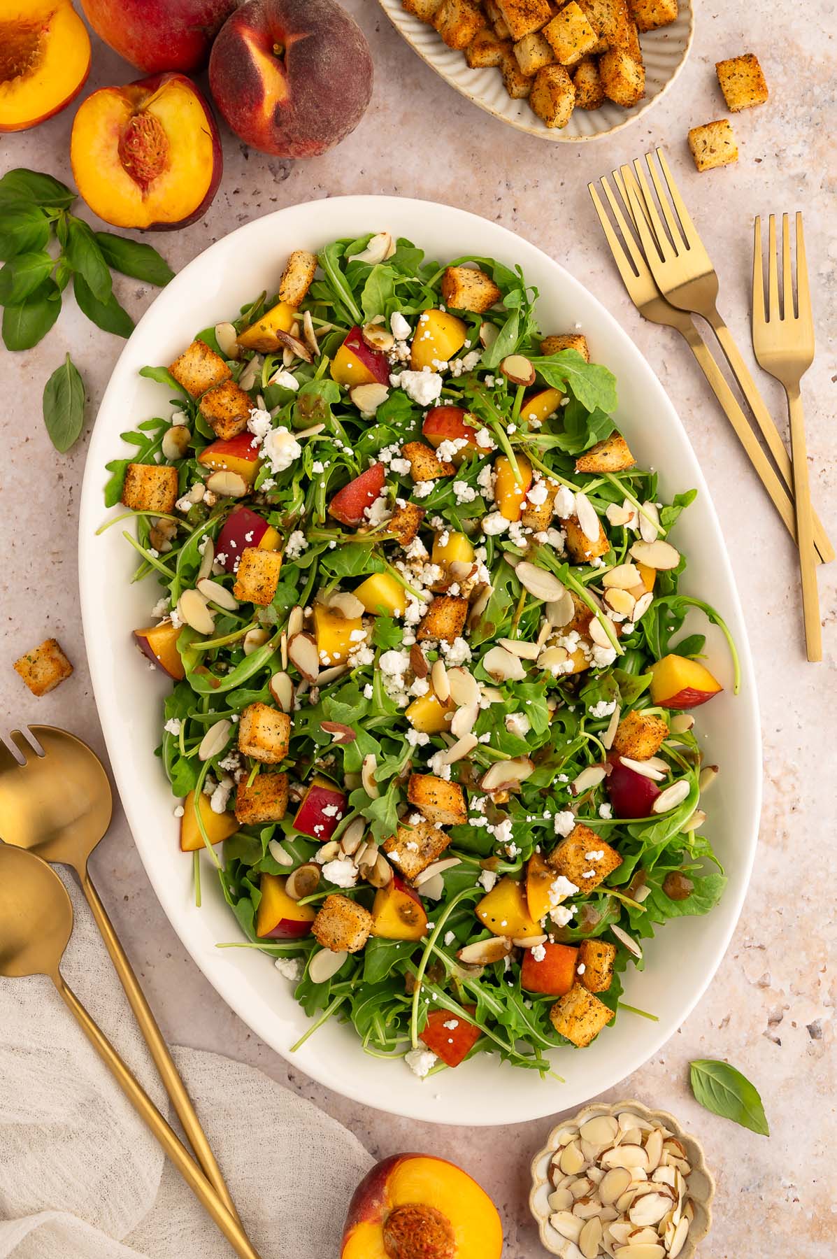 Peach Salad with goat cheese on a large white platter with more fresh peaches on the side.