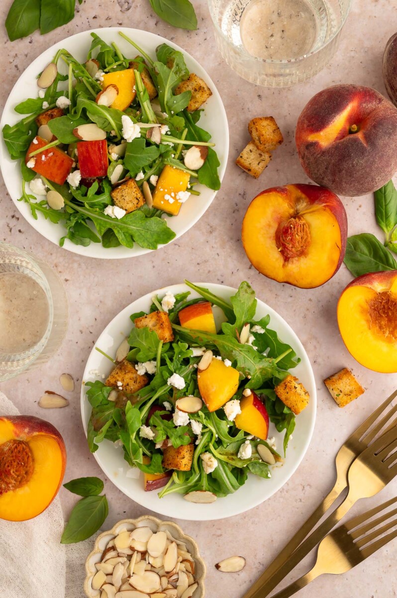 Peach salad with goat cheese on two white plate with more fresh peaches on the side.