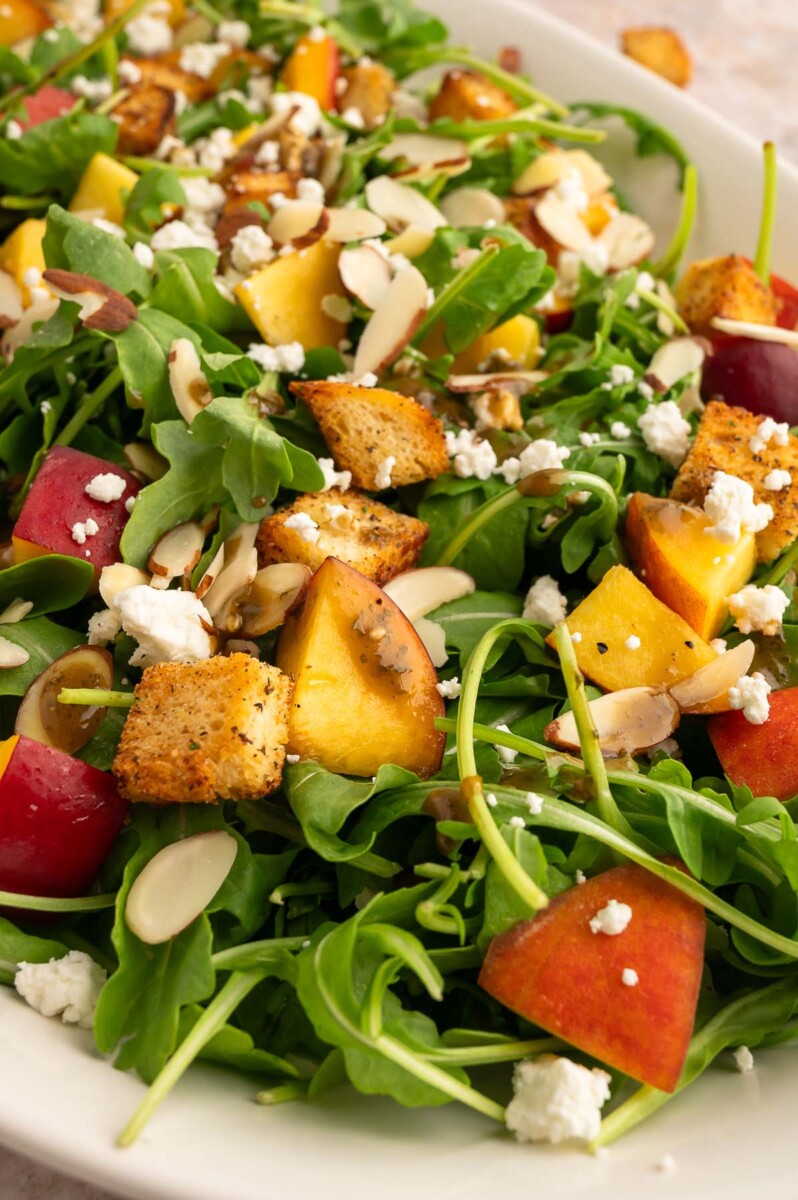 A close up of simple peach salad with goat cheese, homemade croutons, and sliced almonds. 