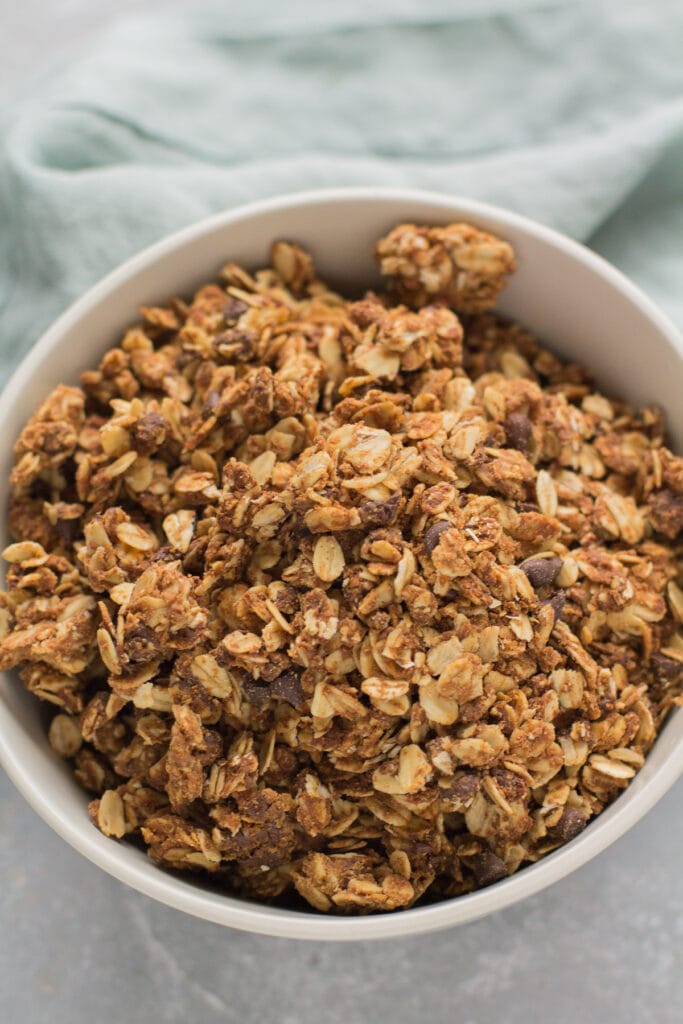 A bowl full of Peanut Butter Granola with a green linen in the back.