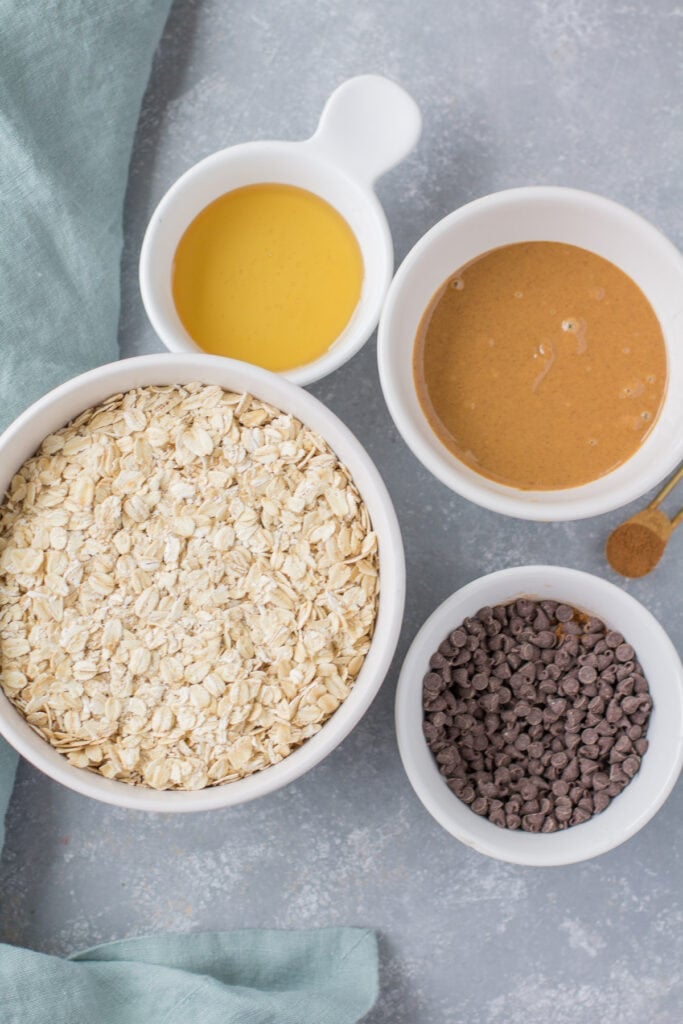 Ingredients for peanut butter chocolate in small white bowls granola on a grey background with a blue linen