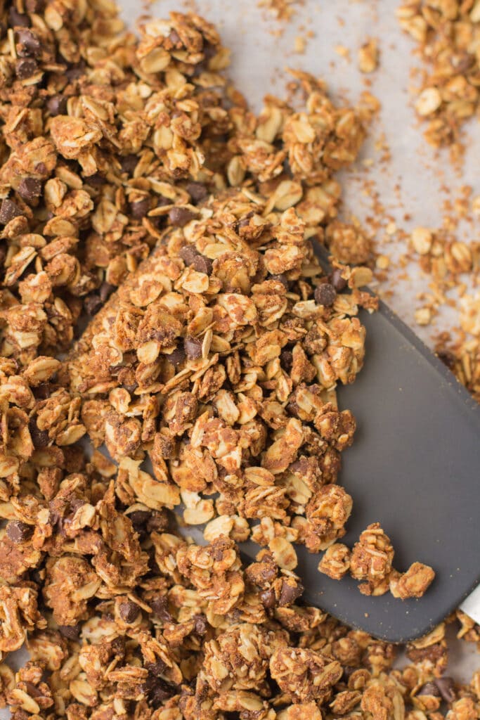 A spatula scooping up some healthy Peanut Butter Granola off of a baking sheet.