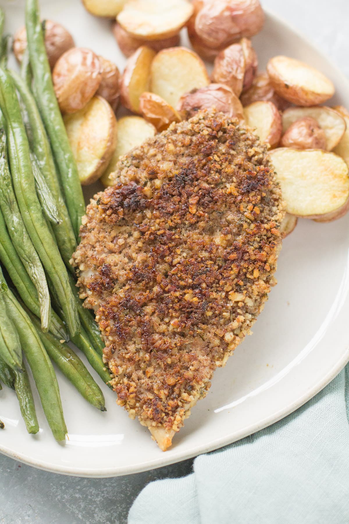 Pecan Crusted Chicken on a white plate with roasted potatoes and green beans.