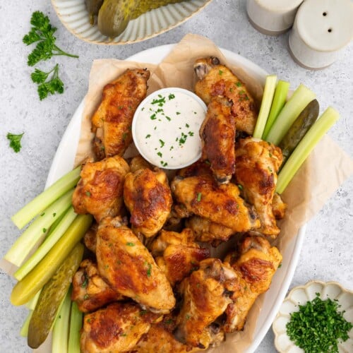 A platter of pickle chicken wings with a small bowl of ranch and celery sticks on the side.
