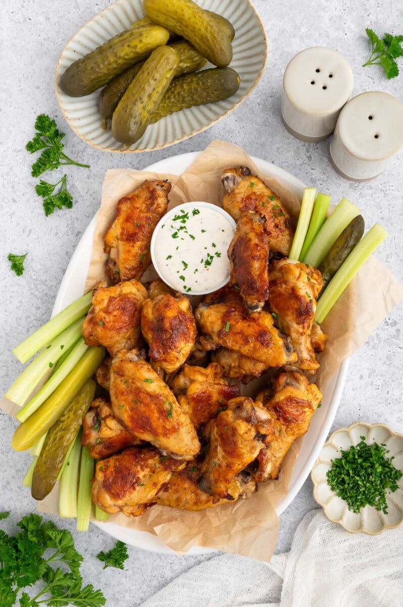 A platter of pickle chicken wings with a small bowl of ranch and celery sticks on the side.