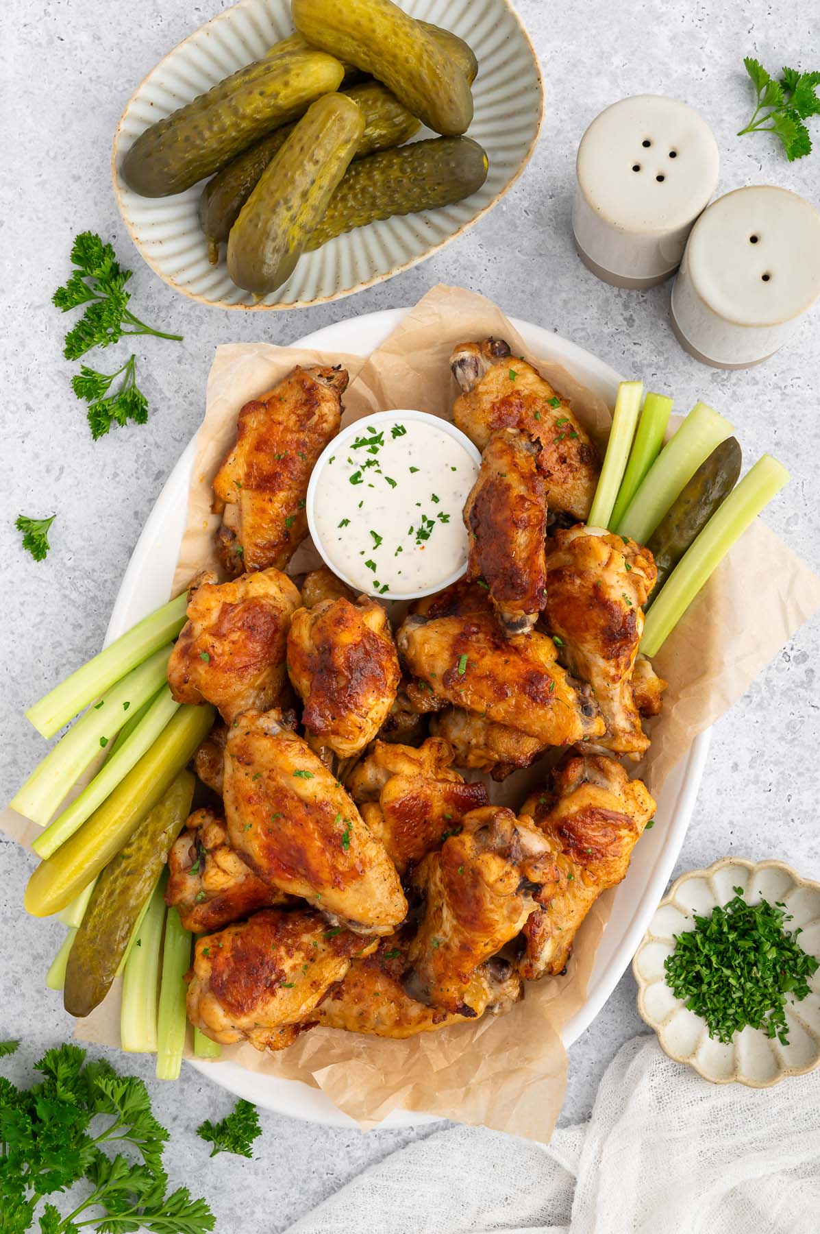 A platter of pickle chicken wings with a small bowl of ranch and celery sticks on the side.