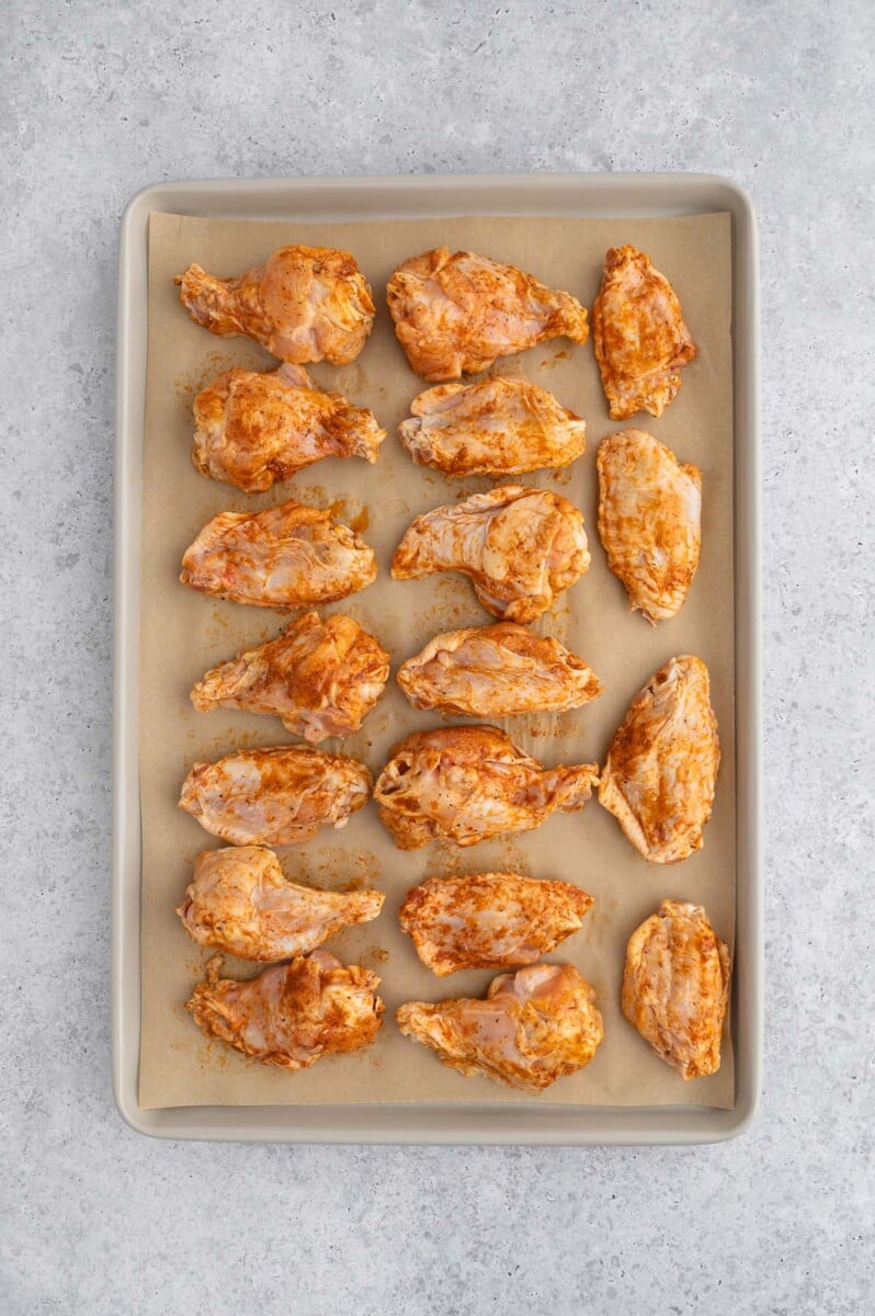 Uncooked pickle chicken wings on a parchment lined baking sheet.