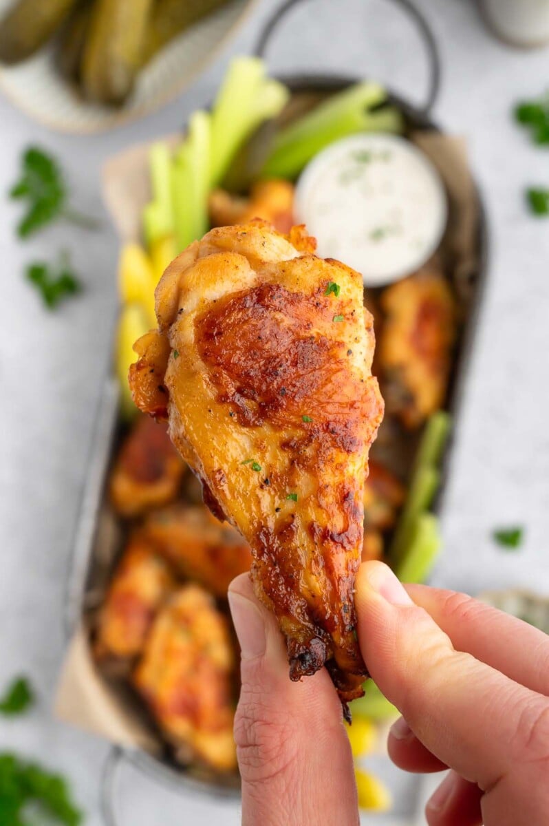 A hand holding up a pickle chicken wing with more wings in the background.