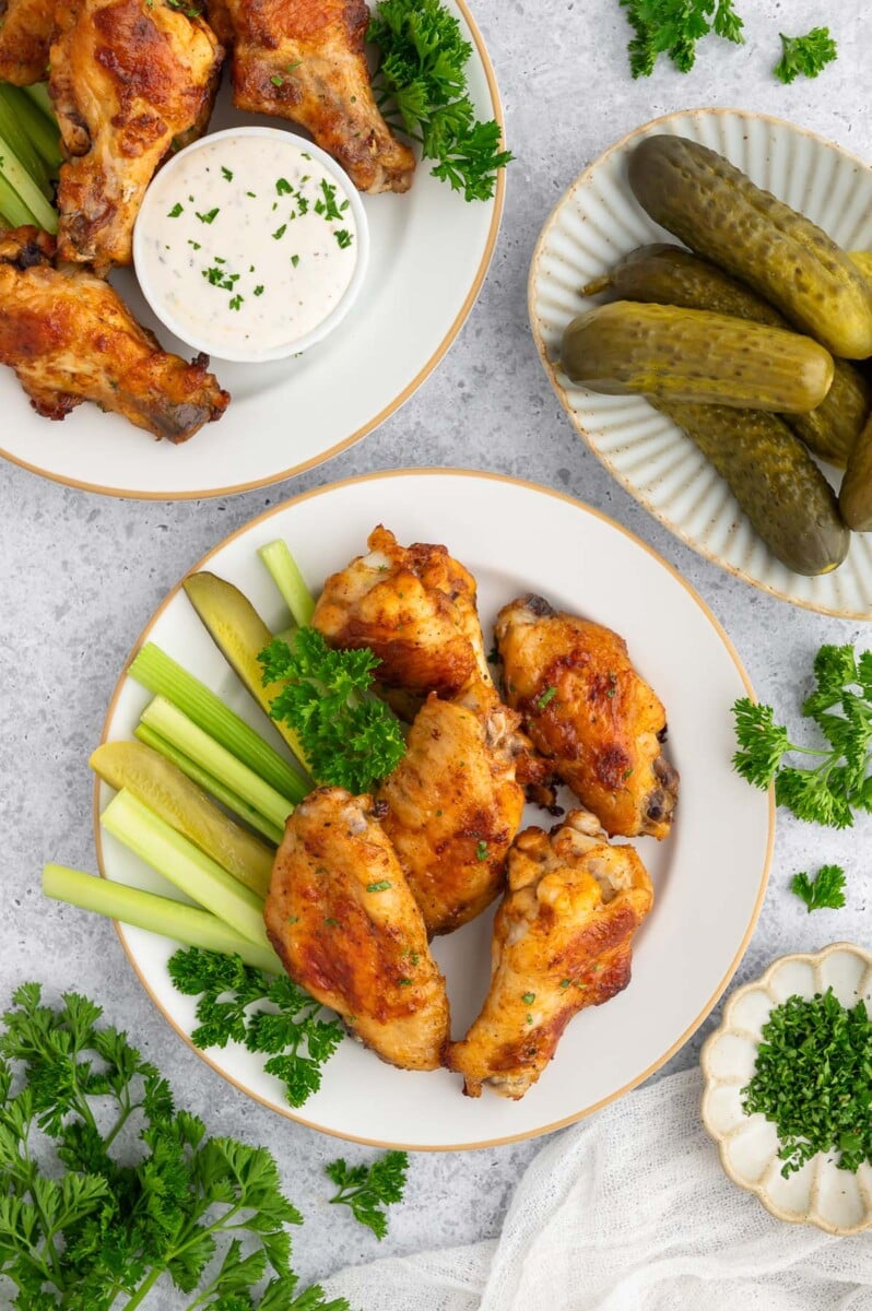 An overhead shot of pickle chicken wings with celery sticks and a plate of pickles on the side.
