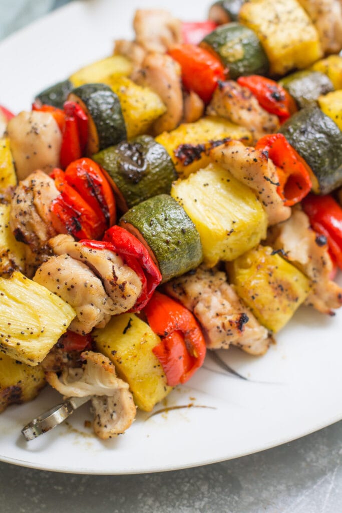 A close up of pineapple chicken kebabs on a white plate