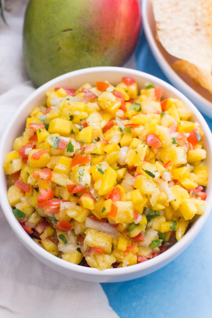 a white bowl filled with pineapple mango salsa on a blue background