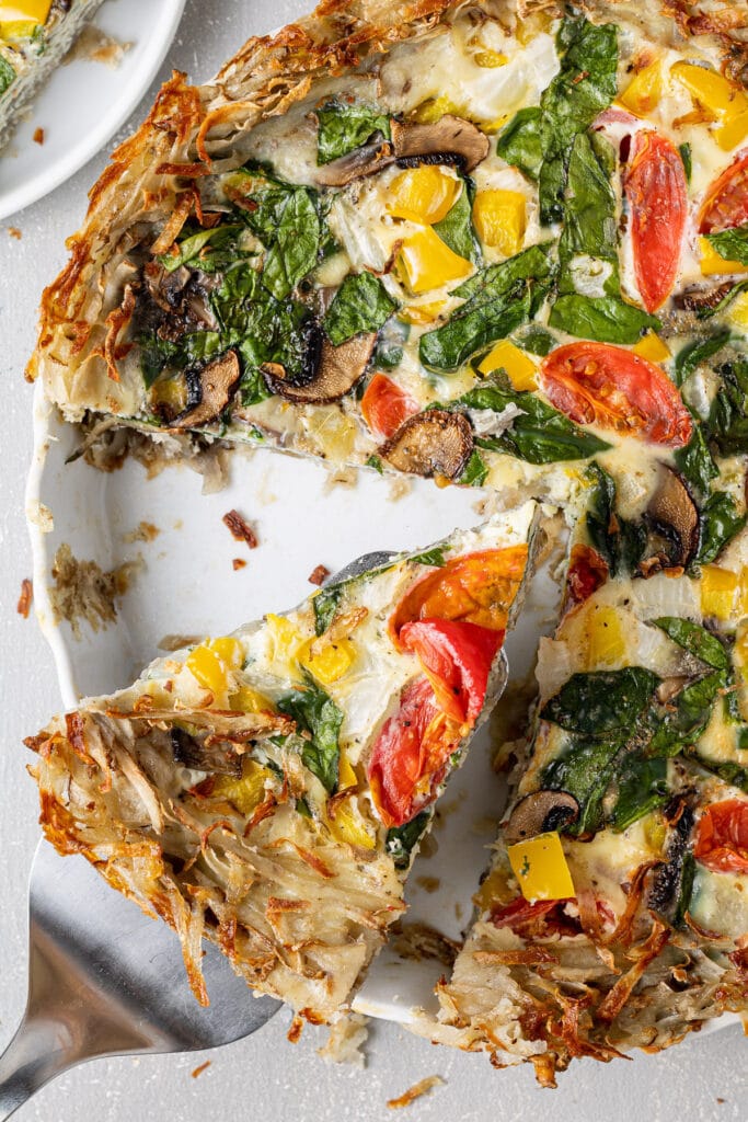 A slice of potato crust quiche being served from a white pie plate