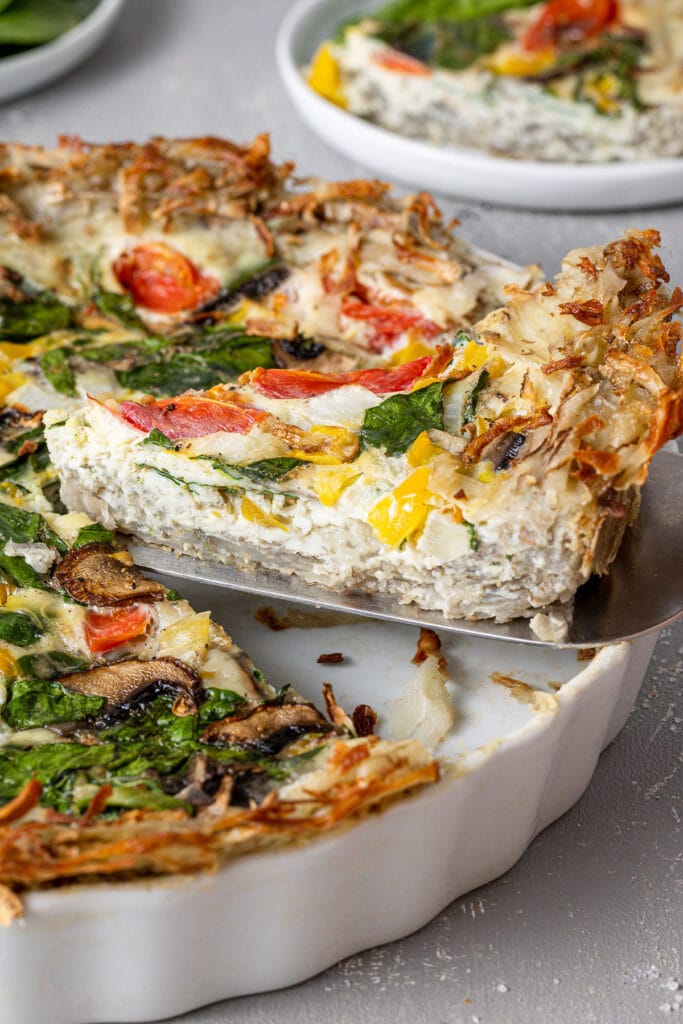 A slice of whole30 potato crust quiche being taken out of a pie plate.
