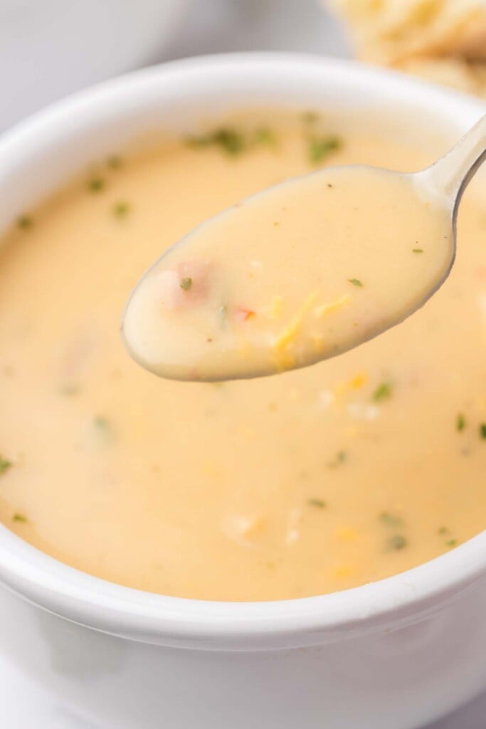 A spoon taking a bite of potato leek soup out of a bowl of the soup in the background.