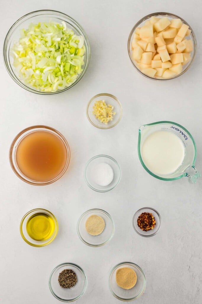 Ingredients for potato leek soup in bowls: olive oil, garlic, leeks, potatoes, vegetable broth, salt, pepper, onion powder, garlic powder, red pepper flakes, dried thyme, dried parsley, milk