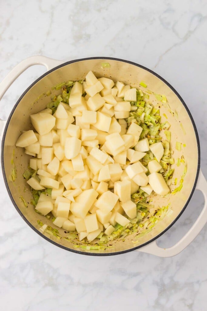 Potatoes added to the top of sautéed garlic and leeks in a dutch oven. 