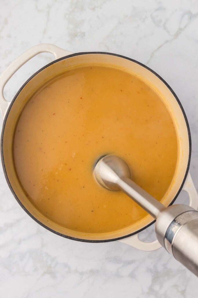 An immersion blender blending up potato leek soup in a dutch oven on a grey background.