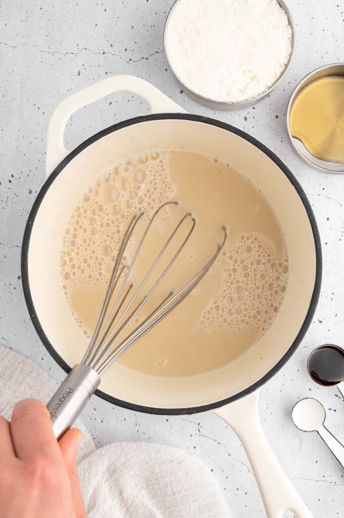 Homemade condensed coconut milk in a saucepan being whisked with more ingredients for protein ice cream on the side