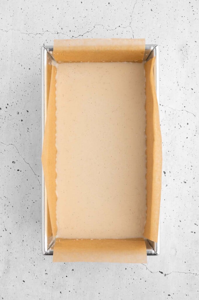Homemade vanilla protein ice cream in a parchment lined loaf pan on a white background