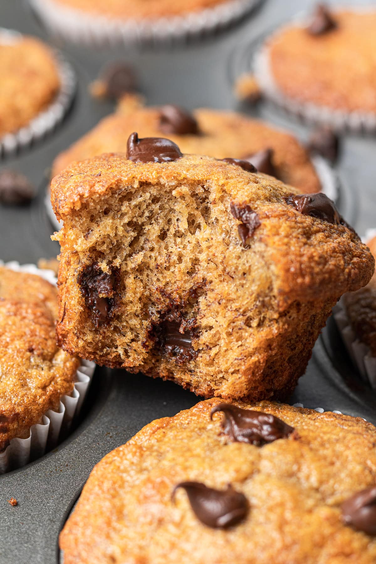 a banana protein muffin with a bite taken out of it sitting on a pan of muffins