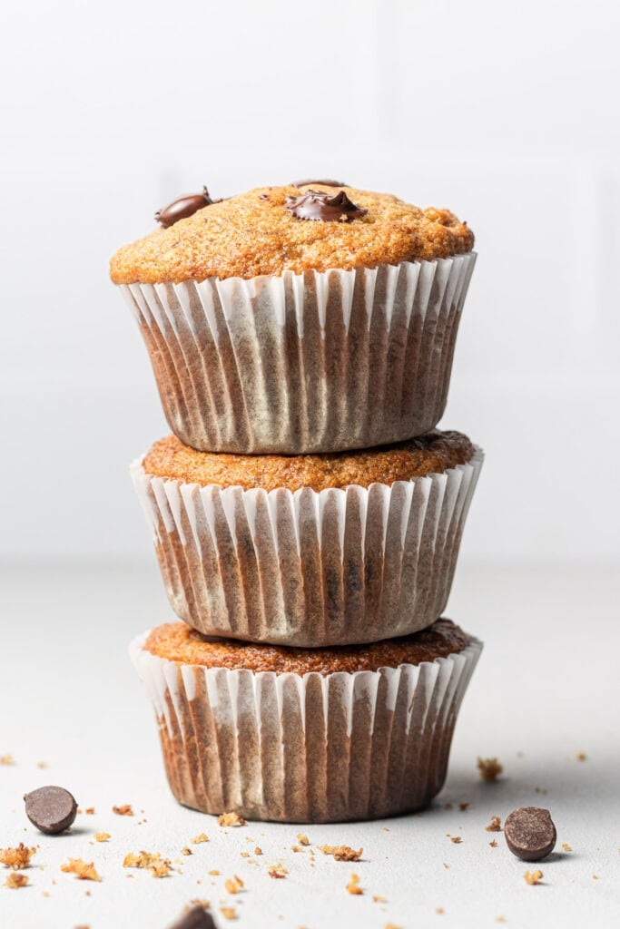 A stack of healthy banana protein muffins with a white background and chocolate chips beside it