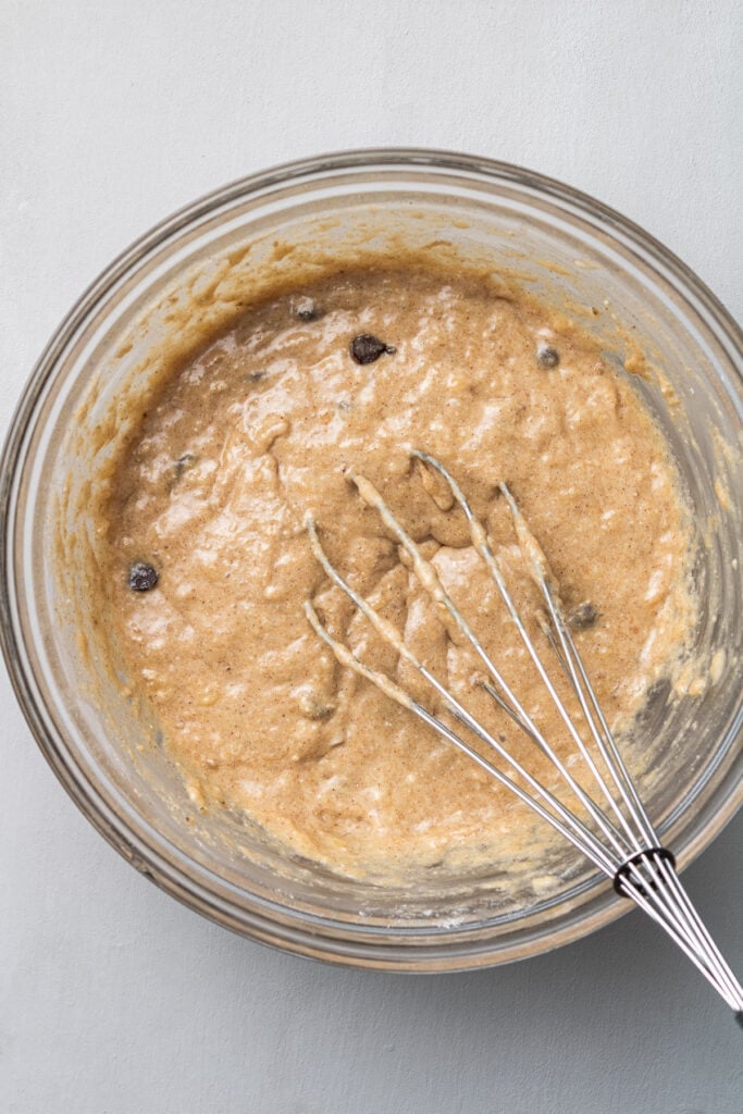 batter for healthy banana protein muffins in a clear glass bowl with whisk in it