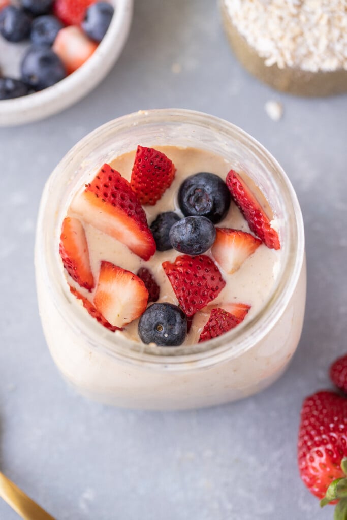 An overhead shot of protein overnight oats with strawberries and blueberries on top with a grey background