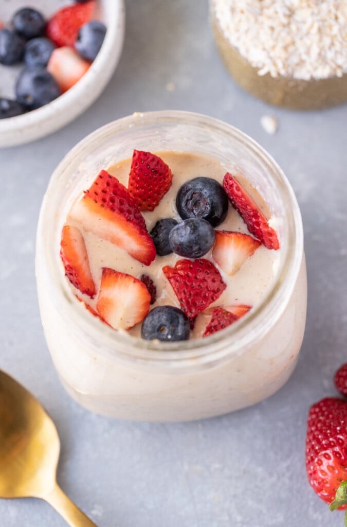 An overhead shot of protein overnight oats with strawberries and blueberries on top with a grey background