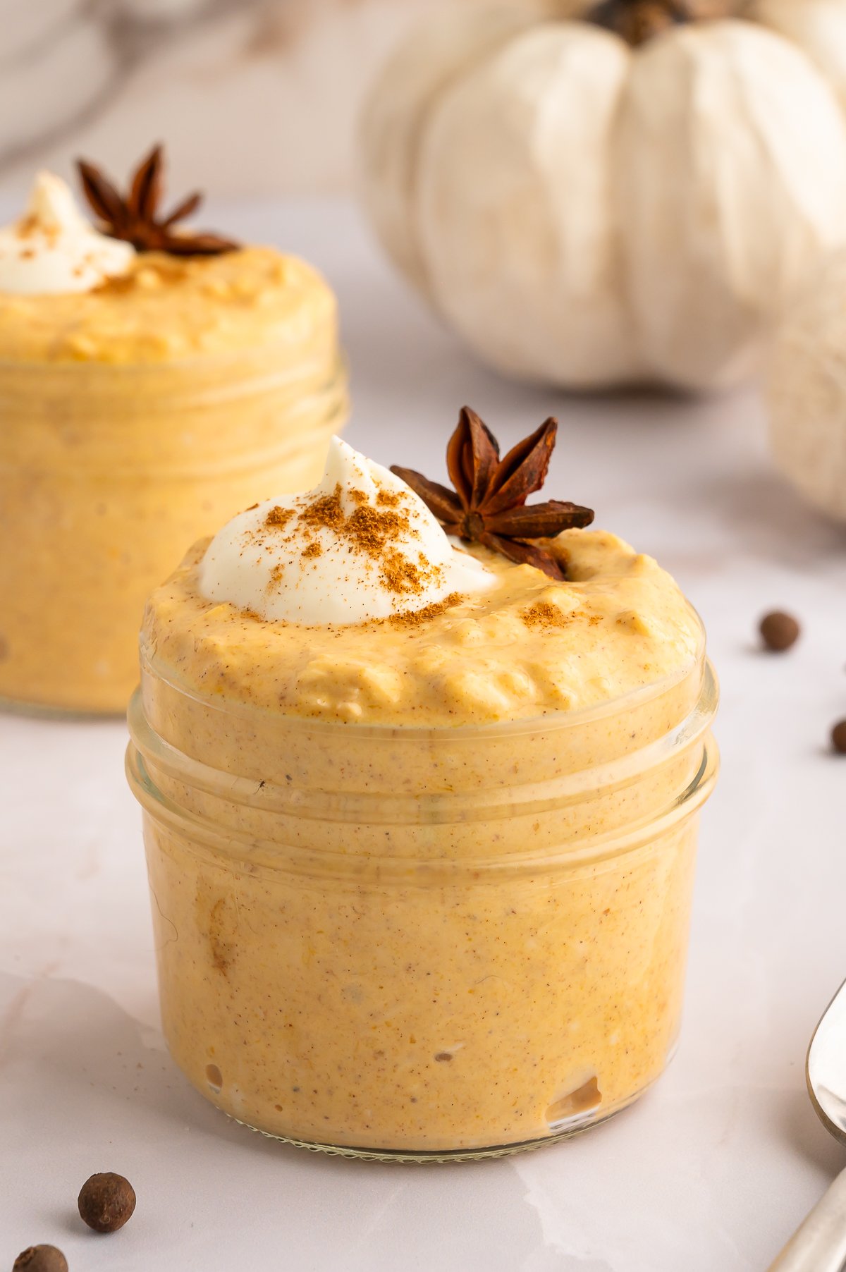 Easy Pumpkin Overnight Oats Recipe in two small clear mason jars topped with cream, pumpkin spice, and a star anise.