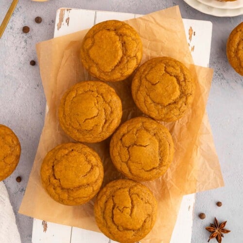 Pumpkin protein muffins on a piece of parchment paper with pumpkin puree in a bowl on the side.