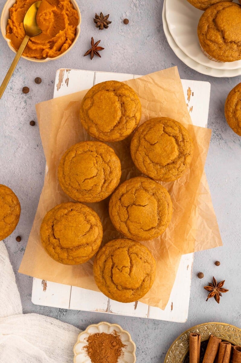 Pumpkin protein muffins on a piece of parchment paper with pumpkin puree in a bowl on the side.