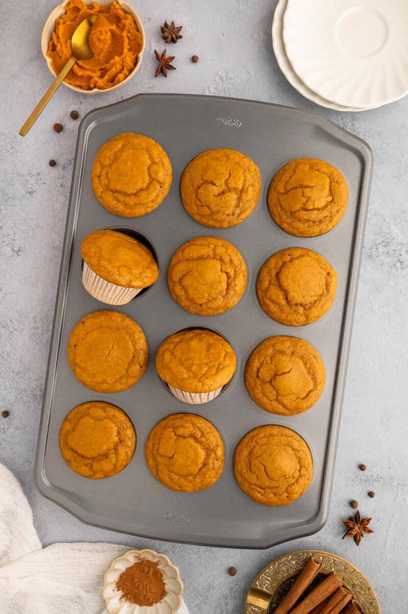 An overhead shot of a muffin tin with pumpkin protein muffins in it with a bowl of pumpkin puree on the side.