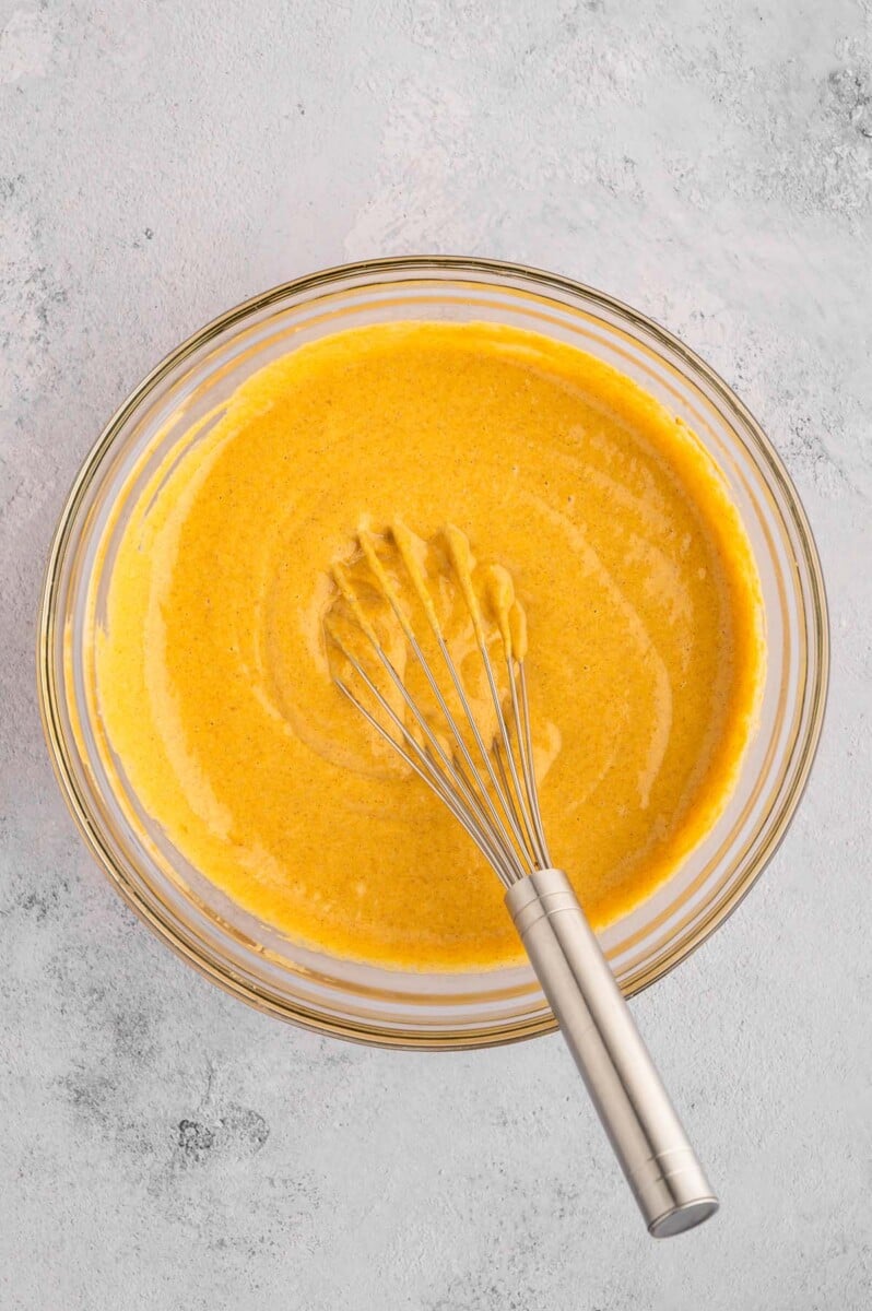 Pumpkin protein muffin batter in a clear bowl with a whisk resting in the bowl.