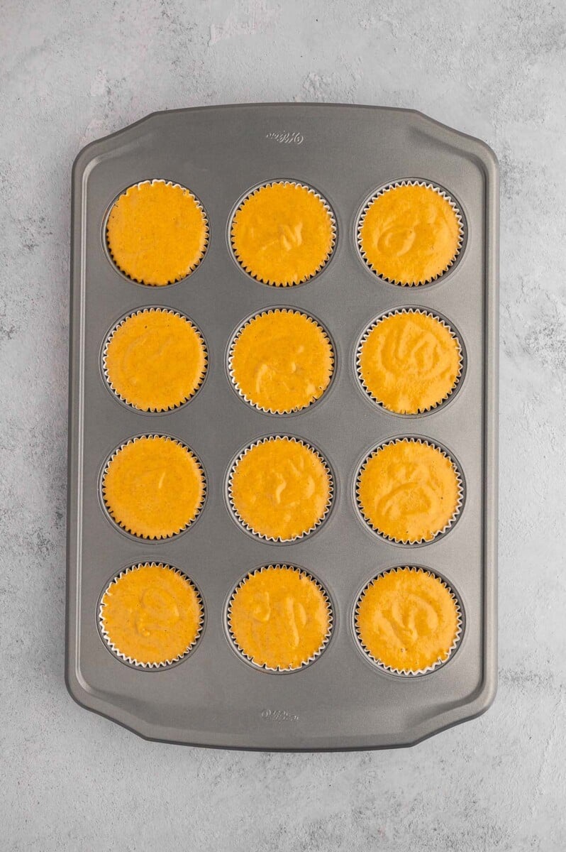 Uncooked pumpkin protein muffins in a muffin tin on a grey background.