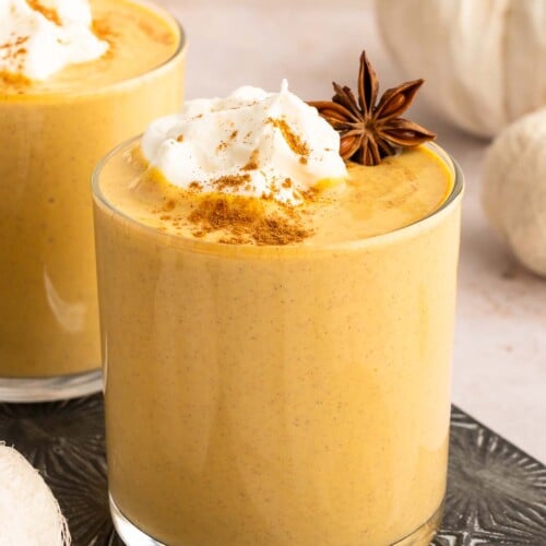 Pumpkin smoothie in a clear glass topped with pumpkin pie spice, whipped cream, and a Star anise garnish.
