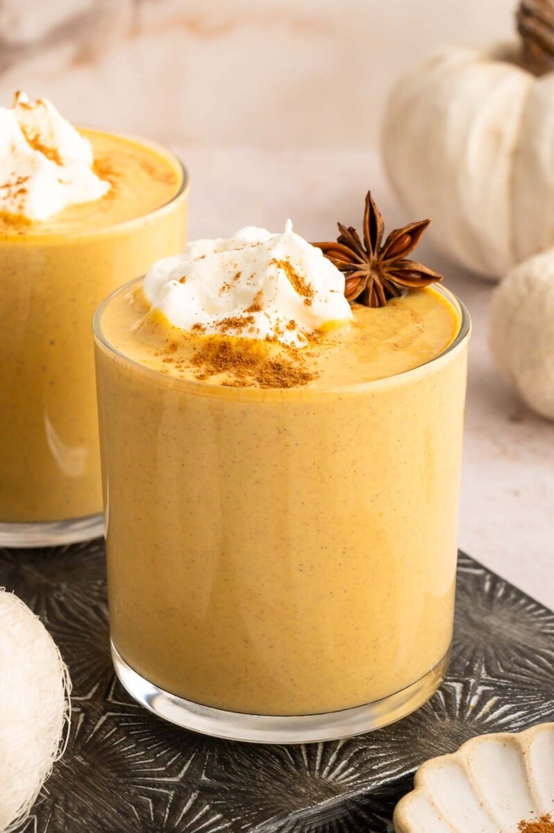 Pumpkin smoothie in a clear glass topped with pumpkin pie spice, whipped cream, and a Star anise garnish.